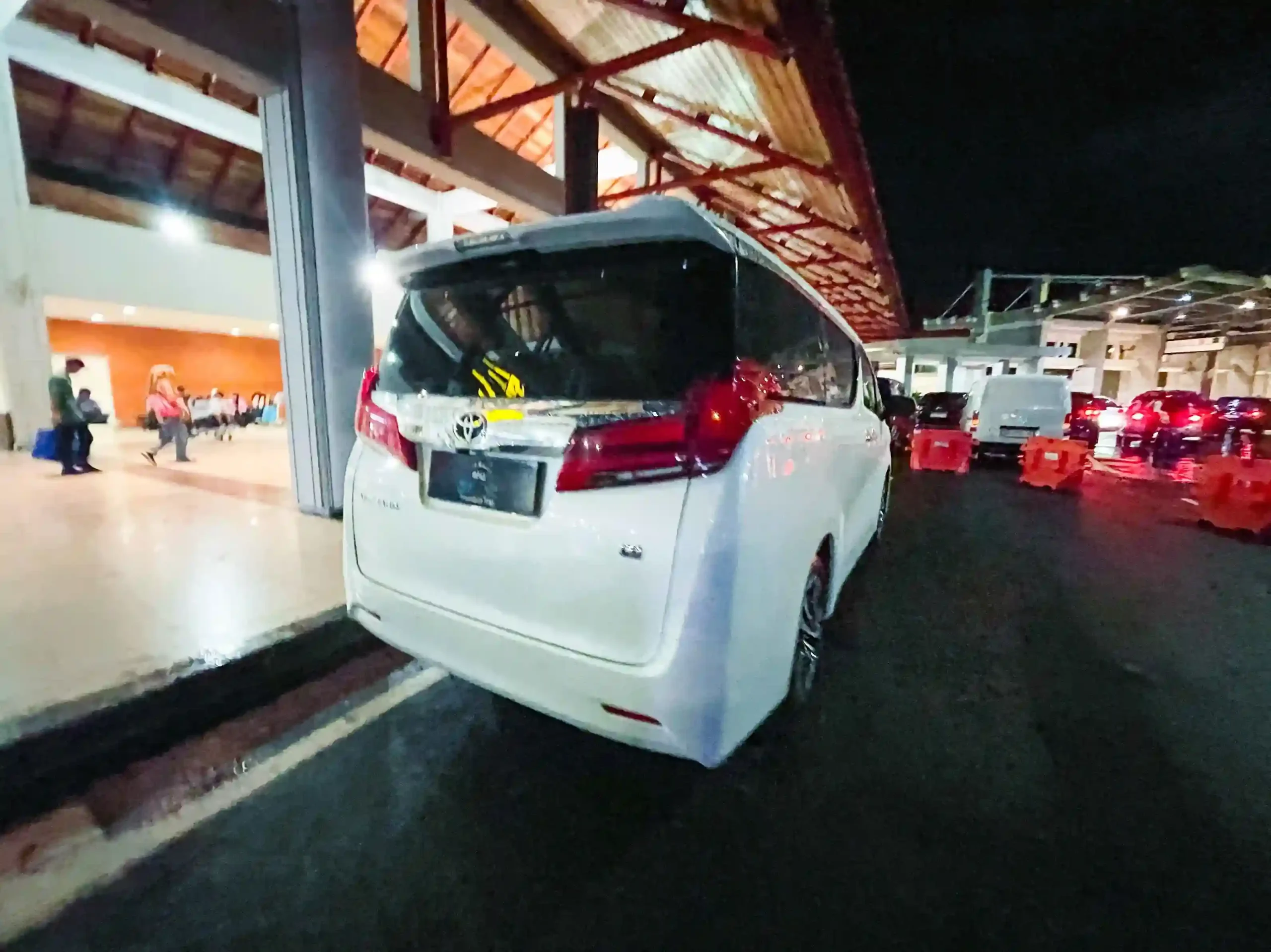白色Toyota Alphard專車夜晚喺峇里島伍拉賴國際機場落客區等候 — 行動不便旅客出閘後可直接上車